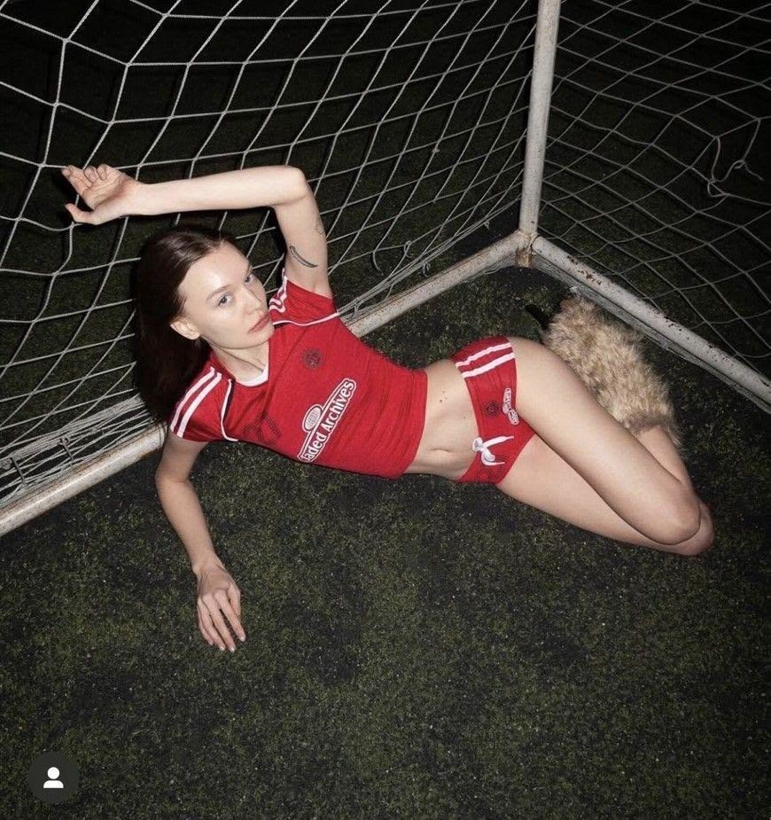 Editorial fashion campaign featuring a model in red sportswear reclining in a soccer goal